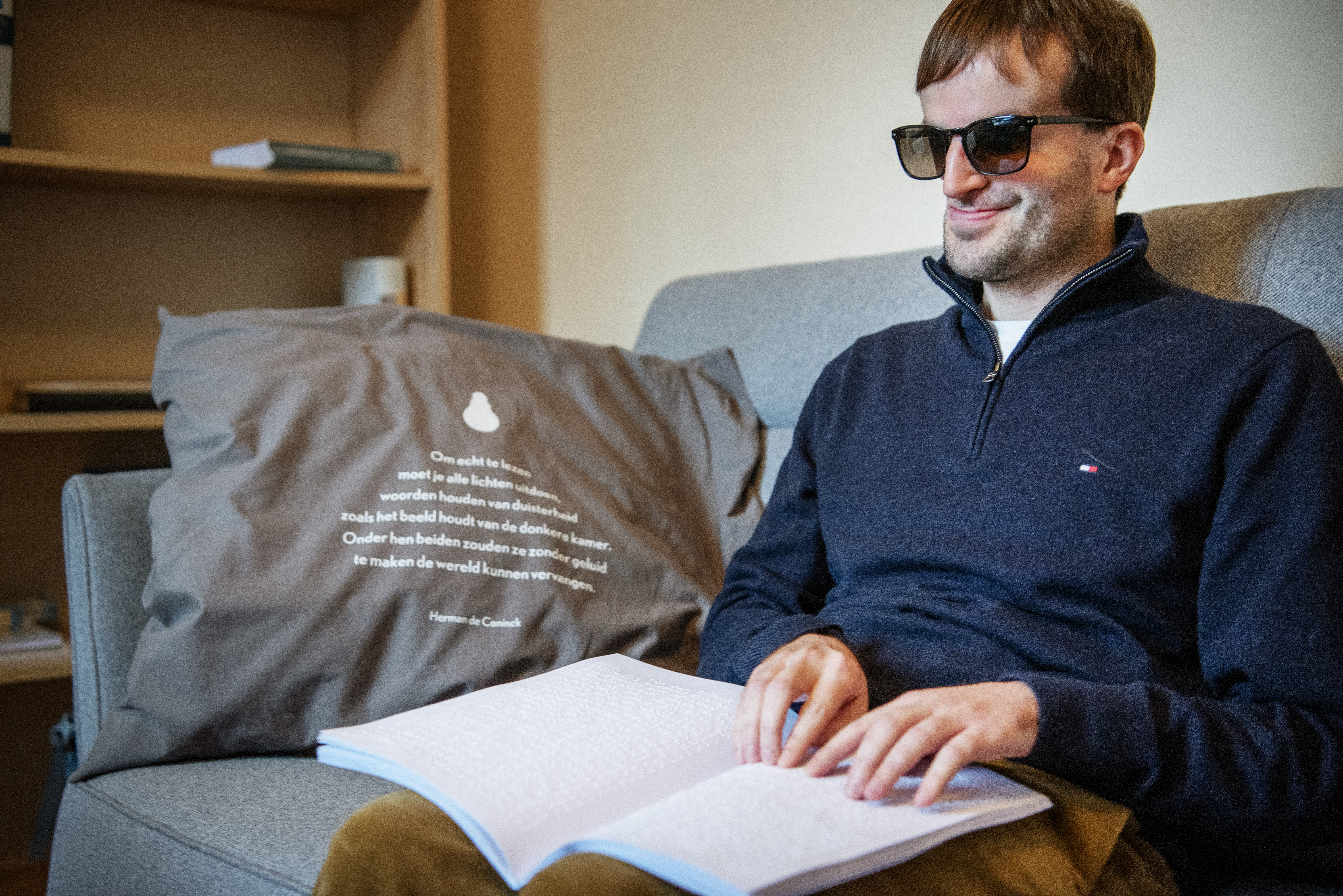 Piet Devos leest een boek in braille in zijn zetel