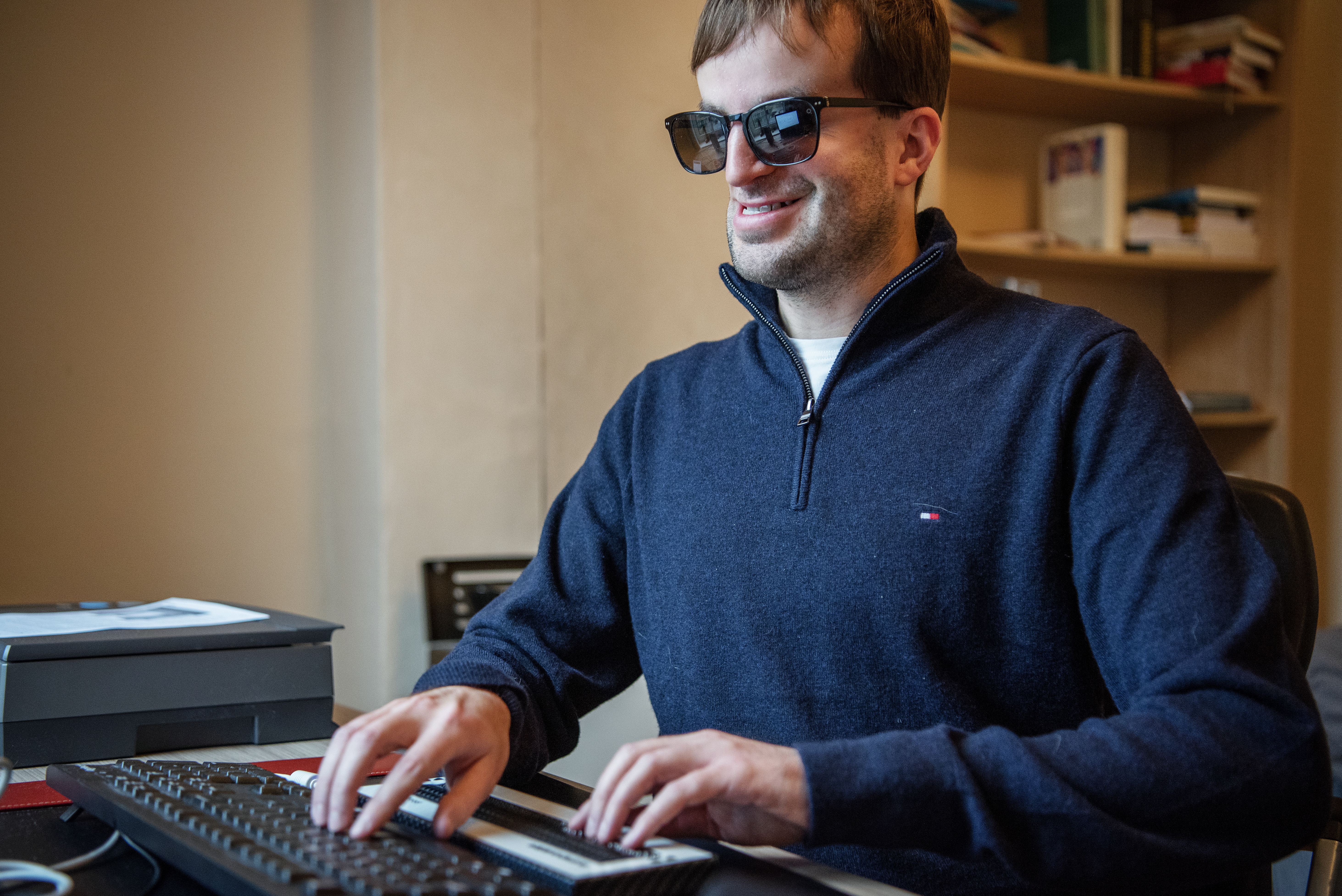 Piet Devos achter zijn bureau met een hand op de brailleleesregel en een op zijn toetselbord